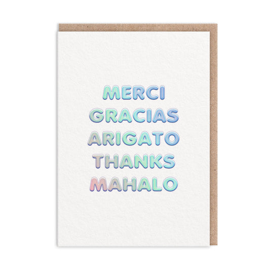 Thank you card with thank you in different languages. Text finished in holographic foil reads "Merci Gracias Arigato Thanks Mahalo"
